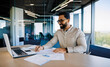 © Pixelowy_czarodziej - A smiling young man in a suit sits in the office at a desk and works on a laptop, typing on a keyboard, texting, working with data