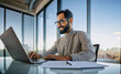 © Pixelowy_czarodziej - A smiling young man in a suit sits in the office at a desk and works on a laptop, typing on a keyboard, texting, working with data