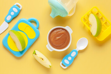 Wall Mural - Apple puree in a bowl and toy plastic tableware. Baby food concept. Top View