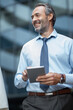 © Panorama - Businessman holding tablet while smiling, corporate district