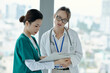 © DragonImages - Young nurse consulting with doctor about diagnosis while they standing in corridor
