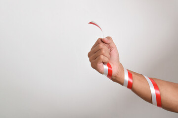 Man's fist with red and white ribbon as a symbol of Indonesian flag, isolated on white background. Indonesian Independence Day concept, August 17th. copy space