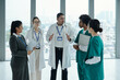 © DragonImages - Team of doctors discussing diagnosis together while standing in hospital corridor