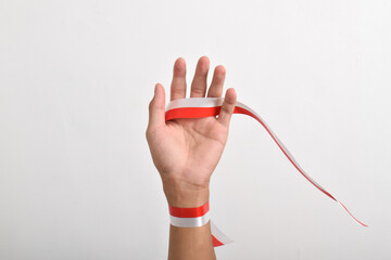 Hand stretched with red and white ribbon as symbol of Indonesian flag, isolated on white background. Concept of Indonesian Independence Day August 17. copy space