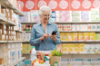 © StockPhotoPro - Happy senior woman buying groceries and using a smartphone
