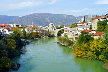 Wall Mural - View of the center of the Bosnian Herzegovinian city of Mostar: Neretva, buildings on the banks of the river, the famous Old Bridge and mountains in the distance. Cityscape from the Lučki most bridge