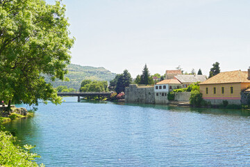 Wall Mural - Summer landscape from the center of Trebinje: the Trebišnjica River, trees, houses of the Old Town on the bank and a mountain in the distance. Tourist places in Bosnia and Herzegovina.