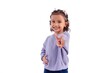 © fadfebrian - A smiling little Asian girl in casual outfit showing two fingers or victory sign, on a white background