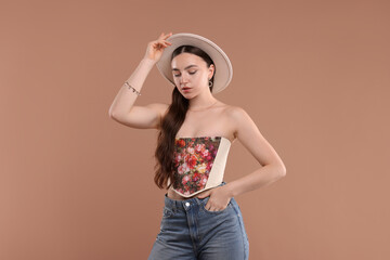 Wall Mural - Beautiful woman in stylish corset and hat posing on beige background