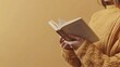 © Thanyaporn - A left-handed person holding a book open with their left hand, reading in a cozy setting. The background is a simple, warm-toned space with ample copy space around the book and hand.