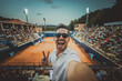 © Davide Angelini - Handsome young tennis spectator taking selfie picture watching grand slam tournament match at the stadium - Sport and technology life style concept