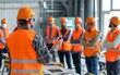 © Ytnart - Construction workers in hard hats and safety vests listen to a supervisor during a meeting.