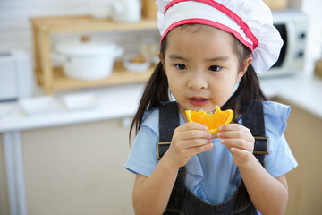 closeup cute asian little child girl eating slice orange in the kitchen