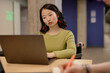 © Seventyfour - Portrait shot of concentrated Gen Z Asian female student studying on laptop during university seminar while sitting at desk in classroom