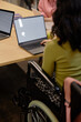 © Seventyfour - Vertical cropped shot of unrecognizable female wheelchair user working on laptop with blank mockup screen while sitting at desk in group class, copy space