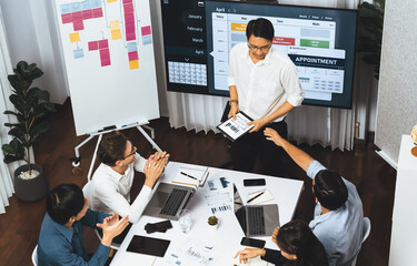 Project manager communicate and collaborate with team using project management software display on monitor, tracking progress of project task and making schedule plan at meeting table. Prudent