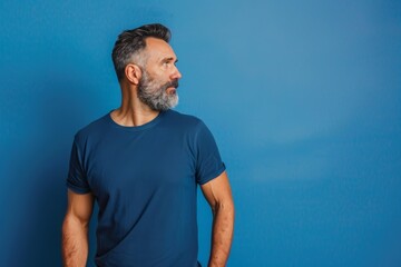 Profile portrait of middle-aged bearded man in blue t-shirt over blue studio background, copy space. Side view of handsome confident man posing on blue, standing straight and looking, Generative AI