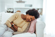 © Dragana Gordic - Woman lying on sofa looking sick in the living room. Beautiful young woman lying on bed and holding hands on her stomach. Woman having painful stomachache on bed, Menstrual period