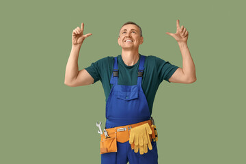 Canvas Print - Portrait of male mechanic with tool belt pointing up on green background