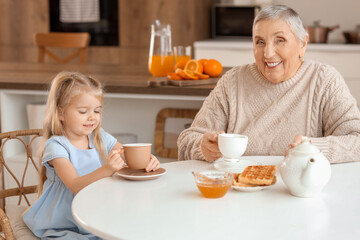 Canvas Print - Cute little girl with her granny having breakfast at table in kitchen