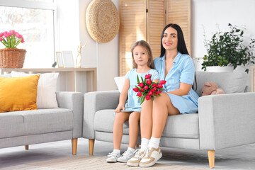 Canvas Print - Happy mother with tulips and her little daughter hugging on sofa at home