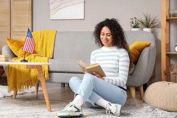 Wall Mural - Young African-American woman reading book with USA flag on table at home