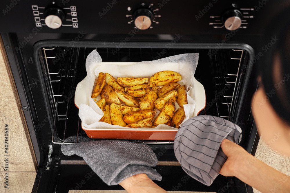 Young woman taking baking dish with potato from oven in kitchen, closeup