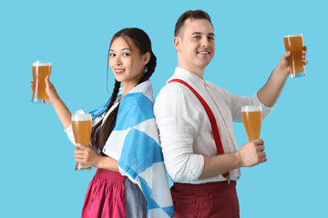 Poster - Young happy couple in traditional German clothes with Bavarian flag and glasses of beer on blue background