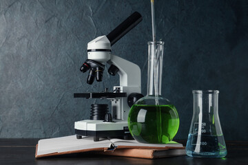 Wall Mural - Modern microscope with chemical flasks and books on wooden table against grey grunge background