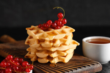 Wall Mural - Delicious Belgian waffles with redcurrant and honey on board on table against black background. Closeup