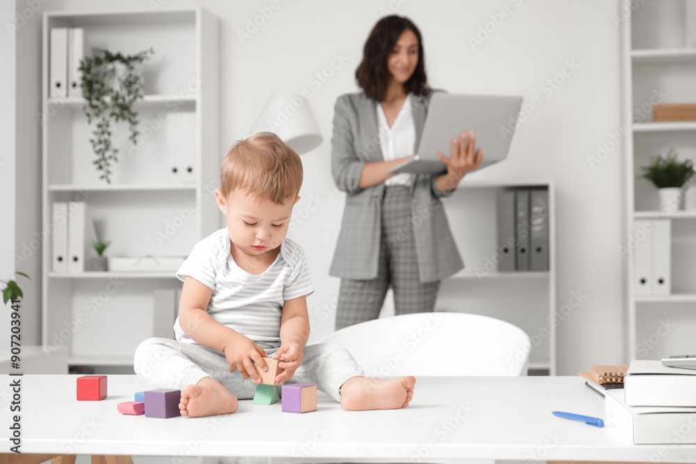 Cute little baby playing with cubes on desk while mother working in office
