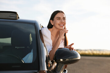 Wall Mural - Smiling young woman leaning out of car window outdoors. Enjoying trip