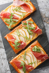 Canvas Print - Puff pastry sandwich with pear, ham and arugula close-up on marble board on table. Vertical top view from above