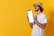 © Morningmaze - Young stylish man standing by huge phone with white empty screen, mockup for advertisement, guy using smartphone, yellow studio background, Generative AI