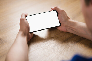 Wall Mural - young man hands holding smartphone with blank white screen in landscape mode