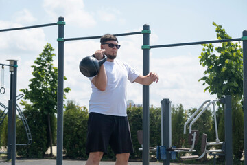 Sportive man workout with kettlebell outdoor in spring or summer