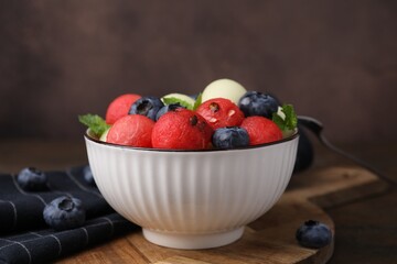 Wall Mural - Tasty watermelon and melon balls with blueberries in bowl on table against brown background, closeup