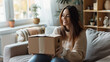 © VK Studio - A young woman is delighted as she opens a package while sitting on a cozy sofa in her inviting, sunlit living room.
