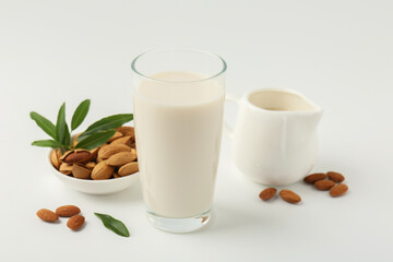 Wall Mural - Fresh almond milk in glass, nuts, green leaves and pitcher on white background