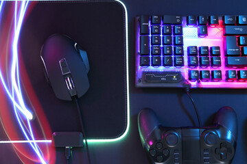 Wall Mural - Computer mouse, RGB keyboard and game controller in neon lights on dark background, flat lay