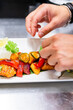 © pavel siamionov - Close-up of a hand garnishing a colorful plate of grilled vegetables with a slice of lemon, highlighting fresh and healthy cuisine