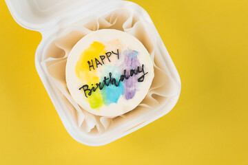 Birthday cake in a white gift box on the yellow background. Little Korean bento cake with happy birthday text. Flat lay