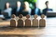 © Worrapol - Wooden Figures Represent a Team: Six wooden figures stand in unity on a table, symbolizing a team against a blurred office background.