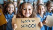 © Neuroshock - Happy elementary students holding sign with back to school writing in classroom and looking at camera