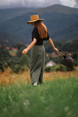 Wall Mural - Fashionable confident woman wearing trendy summer hat, linen shirt, green maxi skirt, holding black wicker straw bag, walking outdoor. Full-length fashion portrait. Rear, back view  