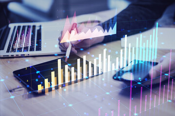 Wall Mural - Person analyzing financial graphs on digital tablet and laptop in office setting.