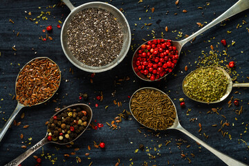 Old spoons with various seeds and spices on black background. Flat lay. Top view. Food concept. Dark mood food photography.