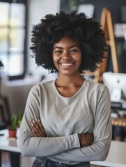 Poster - A woman with curly hair is smiling and standing in front of a desk. She is wearing a gray shirt and has her arms crossed