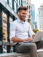 Wall Mural - A man is sitting on a ledge with a laptop in front of him. He is smiling and he is enjoying himself. Concept of relaxation and leisure