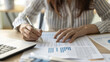 © Pic For You - Close-up of a woman working on financial reports with a pen and laptop, emphasizing productivity and focus.